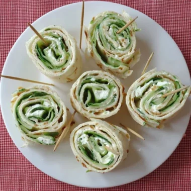 Cucumber and cream cheese sandwich rolls served on a plate.