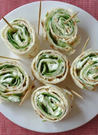 Cucumber and cream cheese sandwich rolls served on a plate.
