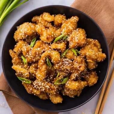Plate of crispy sesame chicken garnished with sesame seeds and green onions