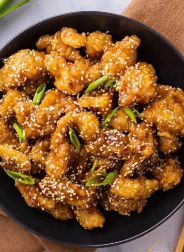 Plate of crispy sesame chicken garnished with sesame seeds and green onions