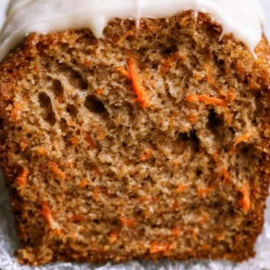 Deliciously moist carrot cake loaf with cream cheese frosting on a rustic table.