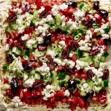 Greek-inspired layered dip with Mediterranean ingredients in a serving dish