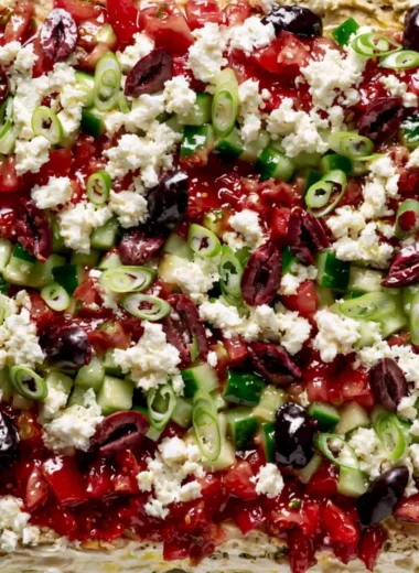 Greek-inspired layered dip with Mediterranean ingredients in a serving dish
