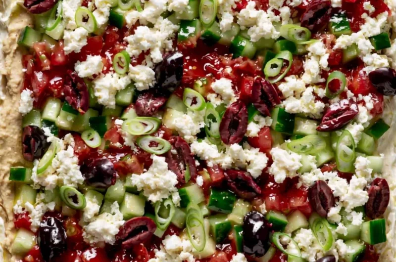 Greek-inspired layered dip with Mediterranean ingredients in a serving dish