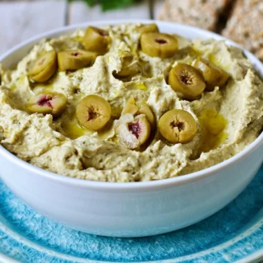 Bowl of olive hummus garnished with olives and herbs