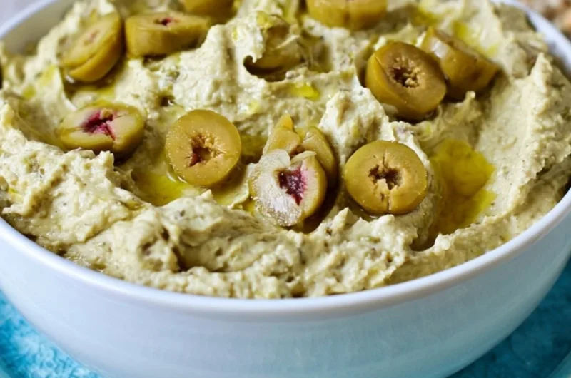 Bowl of olive hummus garnished with olives and herbs